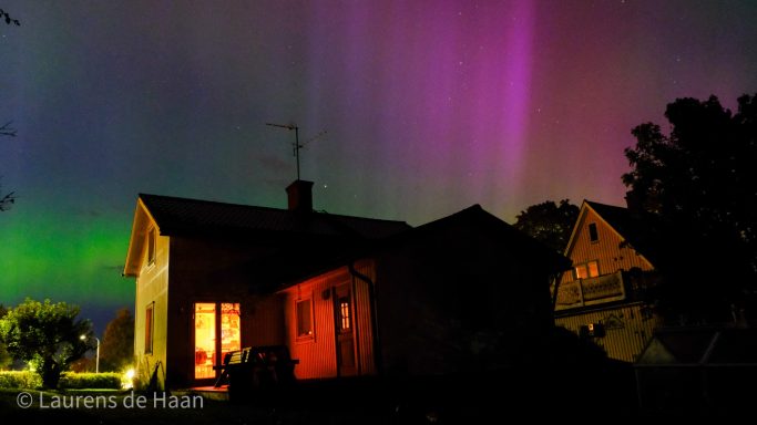 Hus belyst av aurora borealis i färgerna grön, lila och rosa.