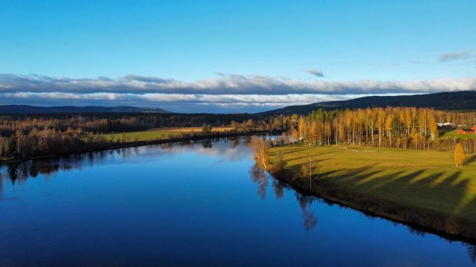 Lugnt vattenspegel med kringliggande grönska och höstfärger i landskapet.