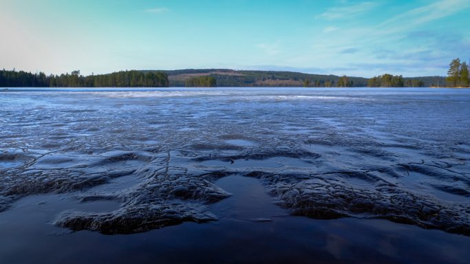 Ett stilla, spegelblanka vattenlandskap med blå himmel och grönskande omgivning.