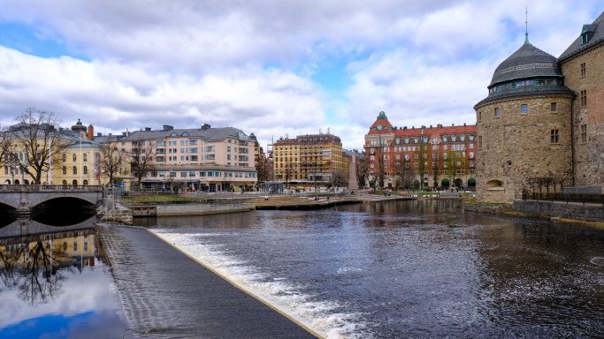 Vy över en stad med vattnet i förgrunden och historiska byggnader i bakgrunden.